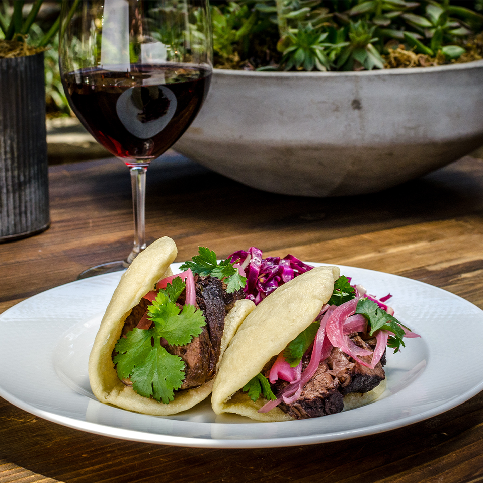 A glass of SIMI Pinot Noir is set next to a plate of pulled pork bao tacos.