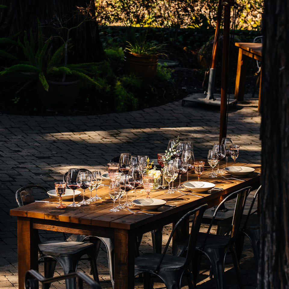 A long table is set outside under the Redwoods on SIMI Winery's patio awaiting guests to start their wine tasting experience.
